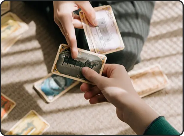 Twee mensen zitten op een tapijt en wisselen speelkaarten met vintage motieven uit, omringd door verspreide kaarten. Zacht zonlicht zorgt voor een warme, ontspannen sfeer.